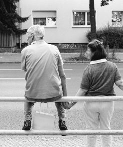 A father waiting for the bus with his daughter, holding her hand because of her physical and mental limitations as she does not see things in three dimensions like others.