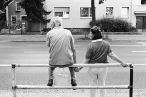 A father waiting for the bus with his daughter, holding her hand because of her physical and mental limitations as she does not see things in three dimensions like others.